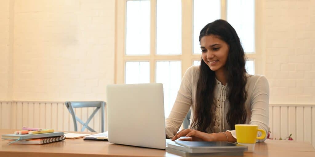 A university student is learning lessons online while sitting at the wooden working desk.